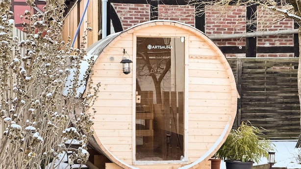 Eine Saune aus Holz mit Glastür, einem kleinen Außenbereich und einer Pflanze in einem Topf in der Nähe.