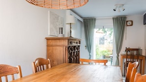 Ein Esszimmer mit Holztisch und Stühlen, einem Holzschrank mit einer Uhr sowie einem Fenster mit Vorhängen.
