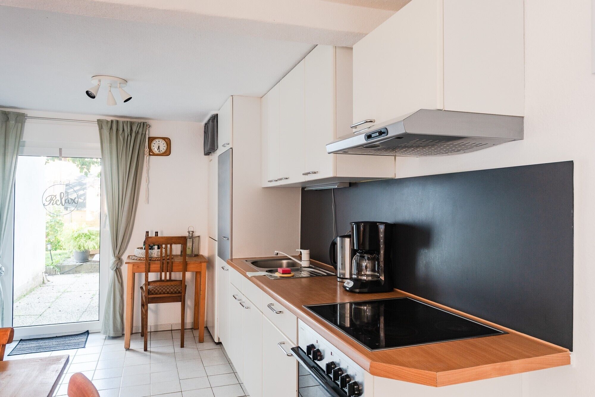 A compact kitchen with a black stovetop, a coffee maker, and a window with curtains.