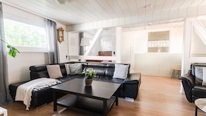 Ein modernes Wohnzimmer mit einem schwarzen Ledersofa, einem Holztisch und einer Treppe, die in eine obere Ebene führt.