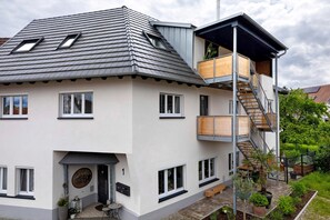 Une maison moderne à deux étages, dotée d’un toit en pente, de nombreuses fenêtres, d’un balcon en bois et d’un escalier menant à l’étage supérieur.