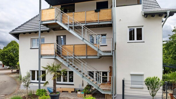 Un edificio residencial de varios pisos con escaleras, balcones y plantas en el exterior.