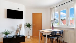 Una sala de estar moderna con televisor de pantalla plana, una puerta de madera, una mesa de comedor con sillas y plantas en macetas.