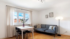 Una habitación con una mesa de comedor, sillas, un sofá, una lámpara de pie y un ventanal con cortinas.