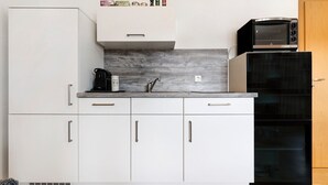 Una cocina compacta con armarios blancos, microondas, cafetera y horno empotrado.