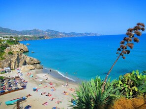 A coastal beach with clear blue water, rocky outcrops, and a variety of beach umbrellas and sun loungers. - Girasol | Golf views - pool - terrace (Mijas Costa)