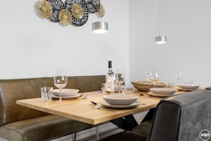 Un comedor con una mesa de madera preparada para cuatro, una botella de vino y una cesta de mimbre.
