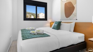 A hotel room with a bed, a window with a view of buildings, a wall-mounted abstract artwork, and a green pillow with the hotel logo. - Santangelo | Sea views - terrace - pool (Benalmádena)