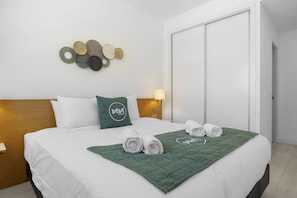 A hotel room with a neatly made bed, a green throw blanket, and a wall decoration.