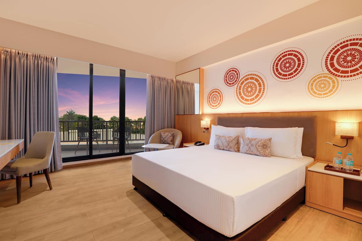 A hotel room with a large bed, a desk, a chair, and a view of the outdoors.