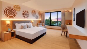 A modern hotel room with a large bed, a desk, a TV, and a large window with a view of the sunset. - Lemon Tree Resort, Somnath (Veraval)