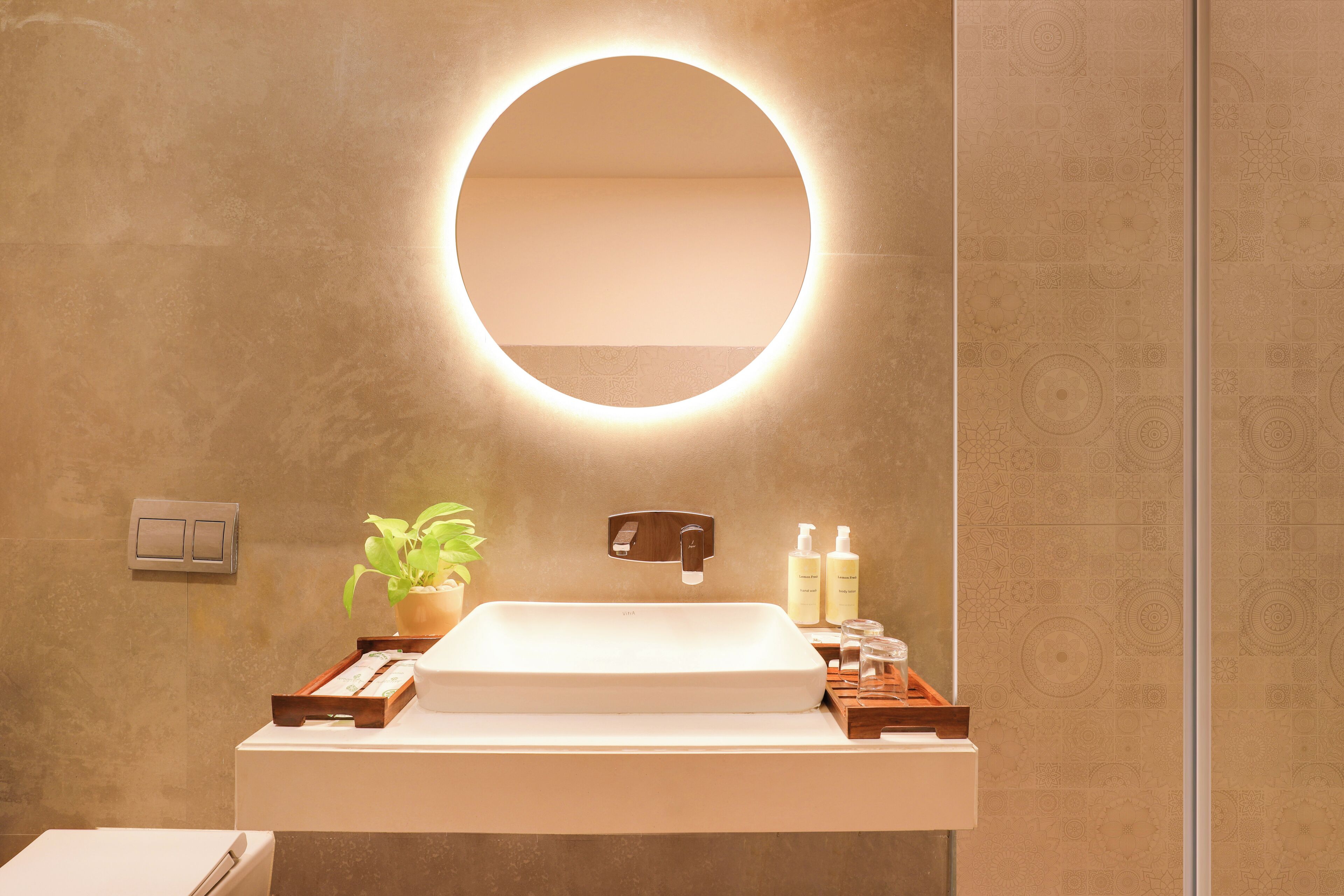Un baño moderno con un espejo redondo, un lavamanos rectangular y una planta en maceta.