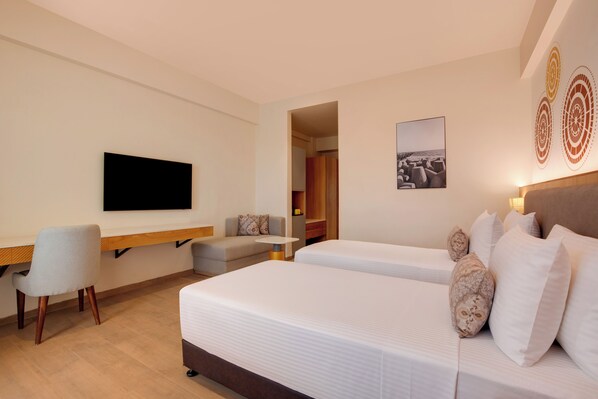 A hotel room with two beds, a desk, a chair, a flat-screen TV, and a painting on the wall. - Lemon Tree Resort, Somnath (Veraval)