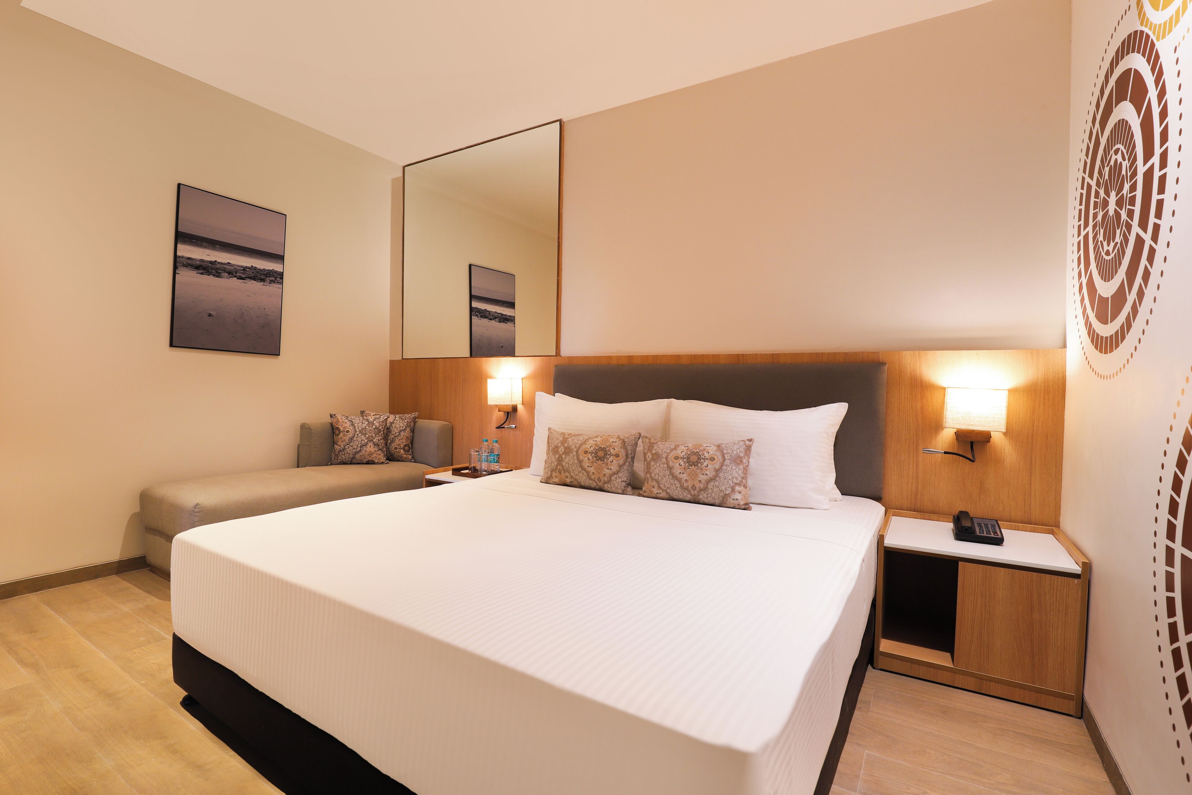 Una habitación de hotel con una cama grande, mesitas de noche con lámparas, un sofá y un espejo montado en la pared.