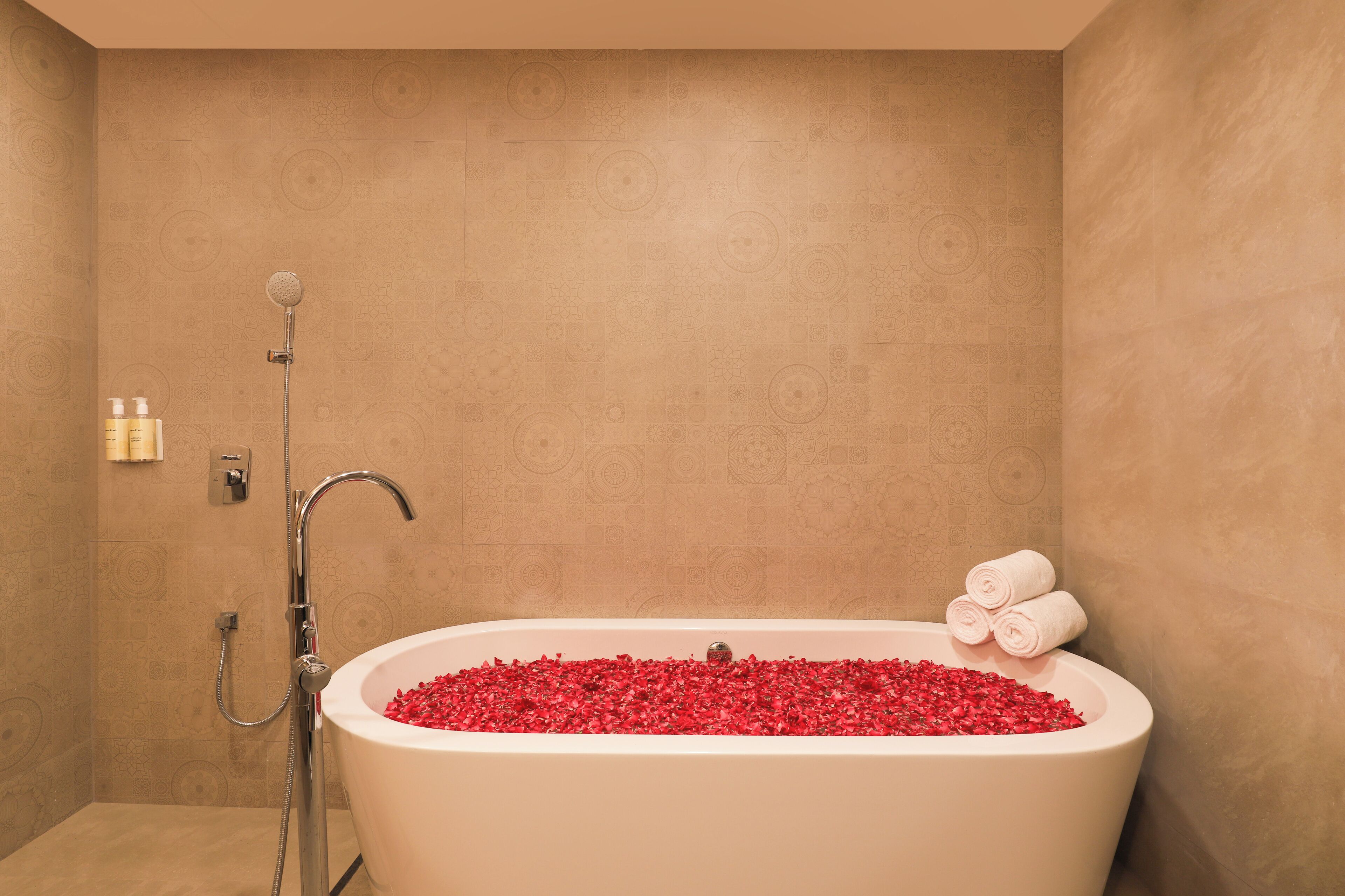 A bathroom with a bathtub filled with red bath beads, a showerhead, and a towel rack with towels.