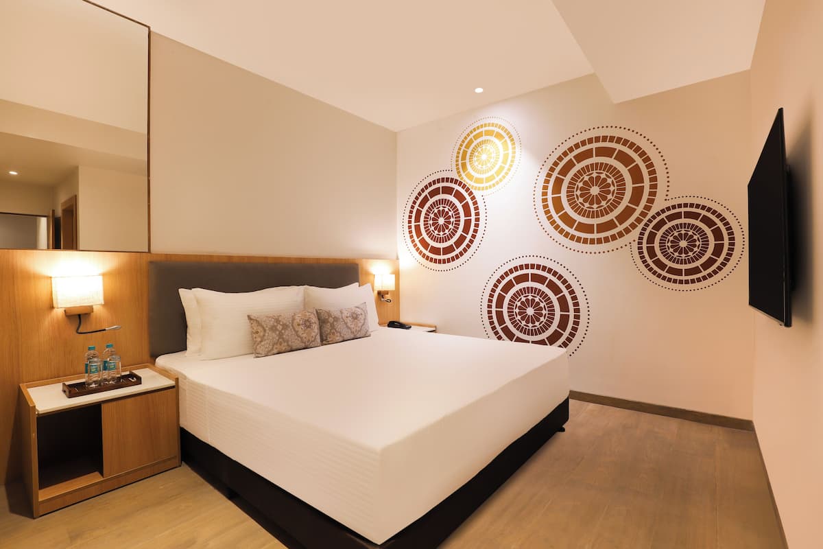 A hotel room with a large bed, a bedside table with a lamp, and a wall-mounted TV.