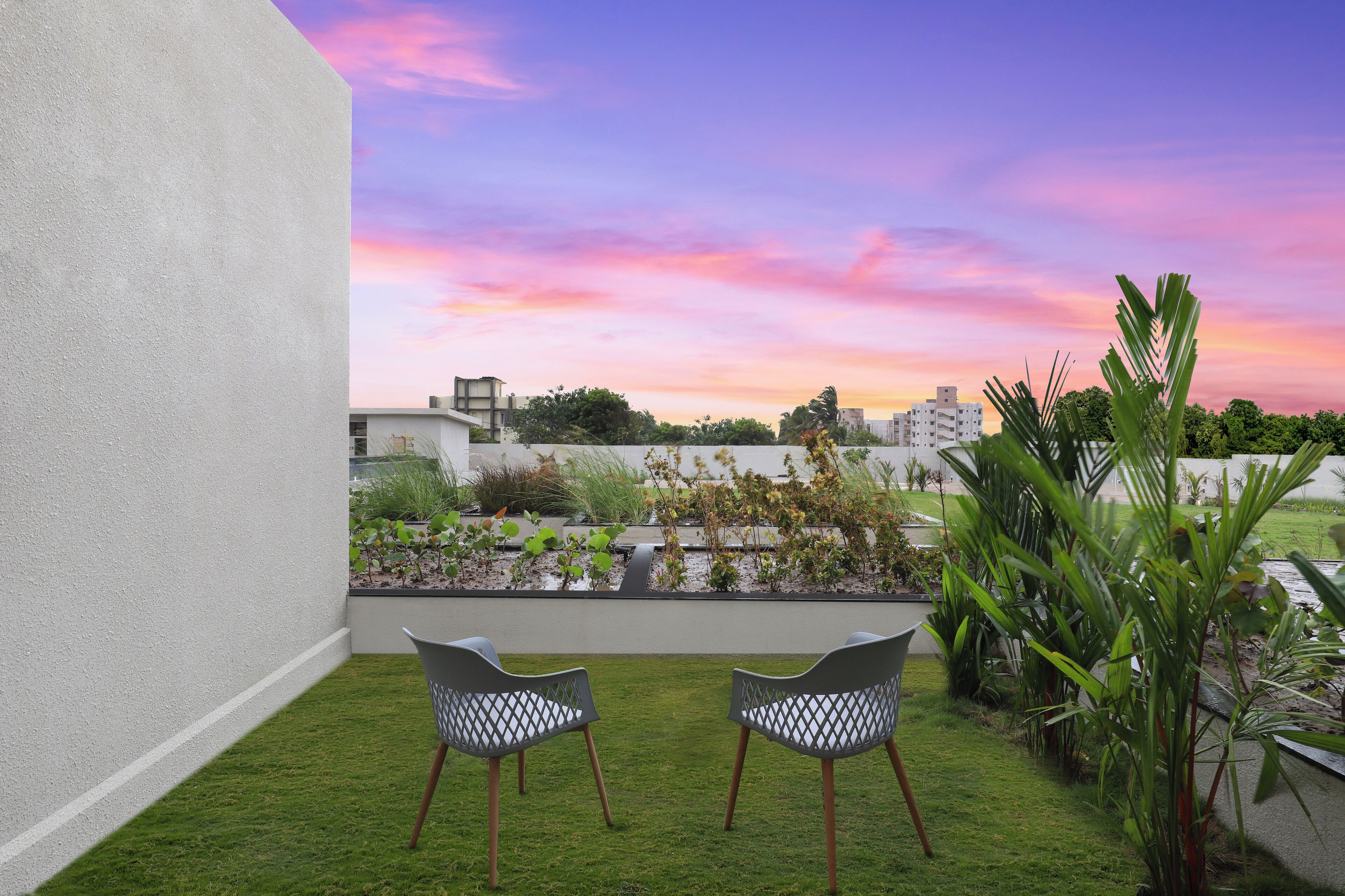Una terraza en la azotea con dos sillas, un pequeño jardín y vistas a edificios bajo un cielo al atardecer.