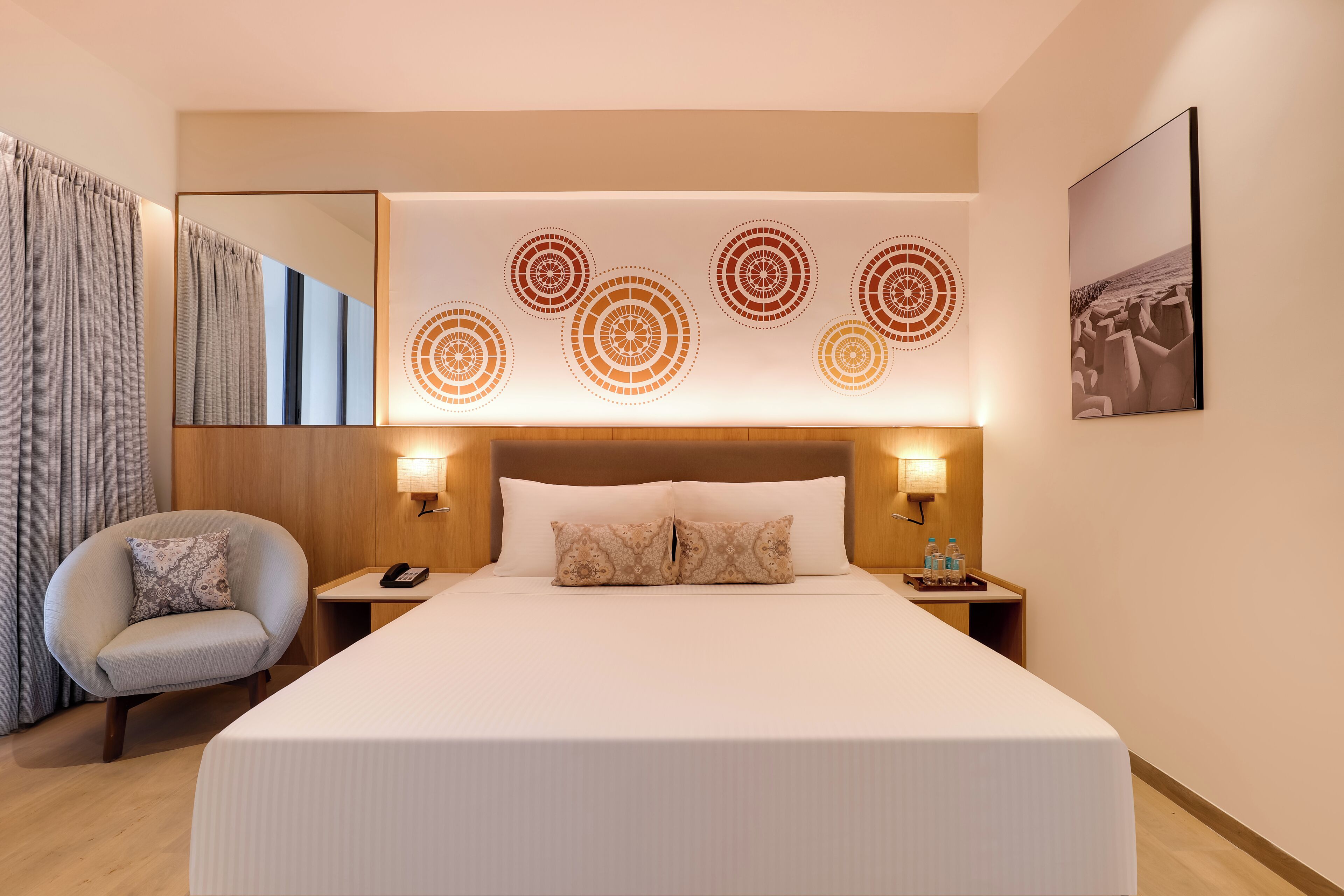 Une chambre d’hôtel moderne avec un grand lit, une chaise, une table de chevet avec un téléphone et une œuvre d’art murale.