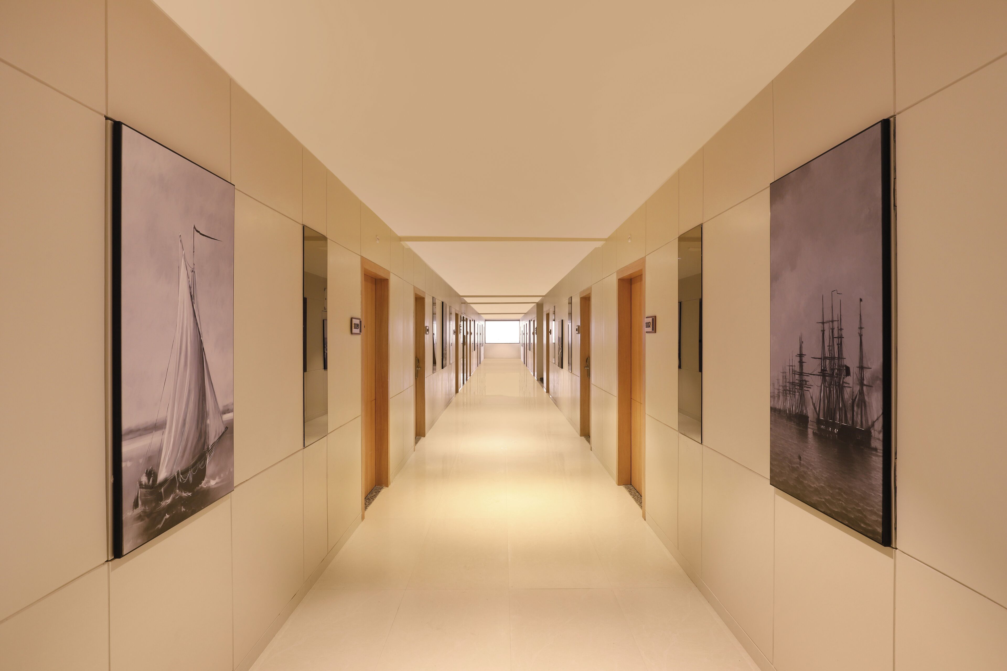 A long, narrow hallway with a series of doors on either side, each with a framed picture above it.