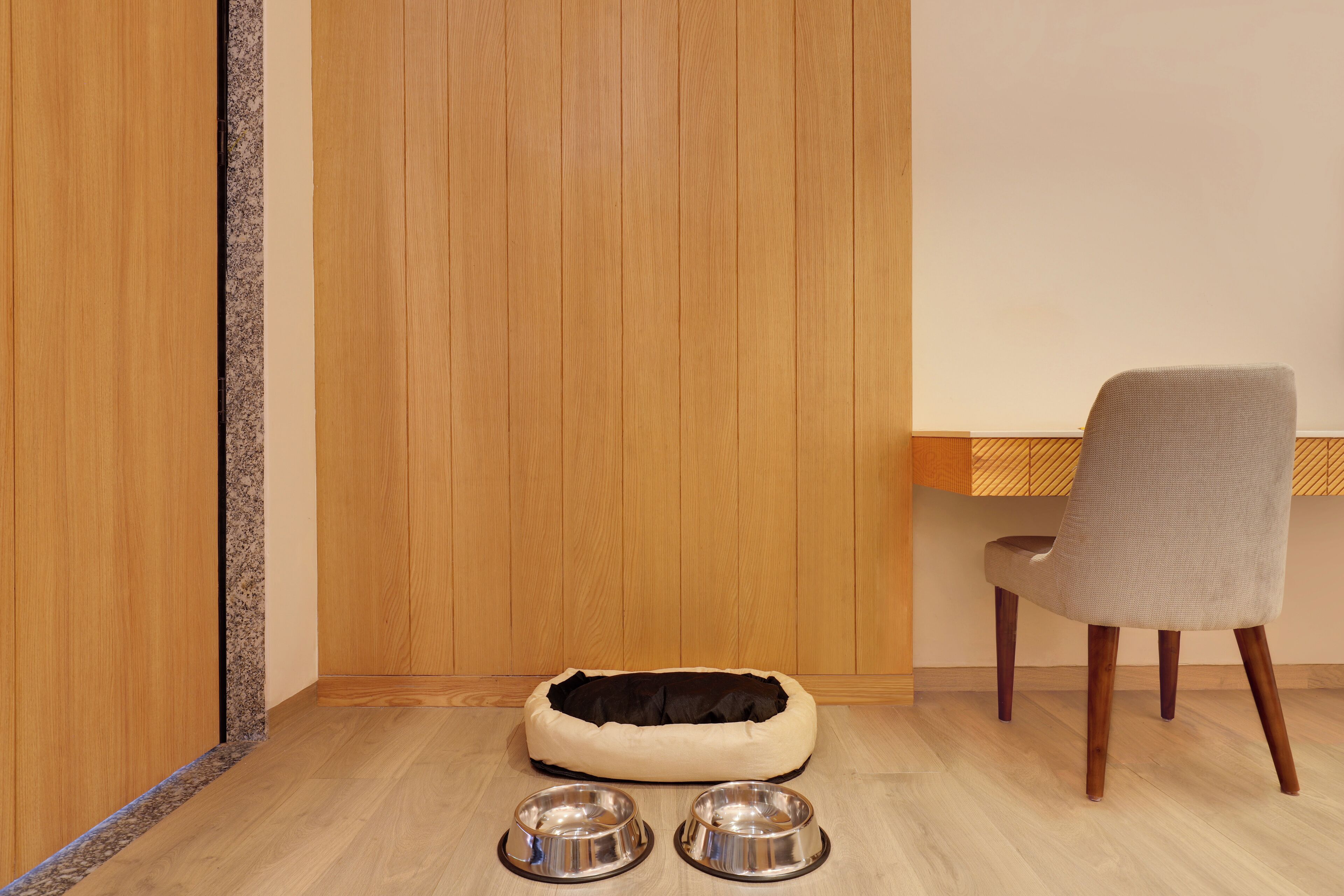 A pet bed and two metal bowls on a wooden floor.