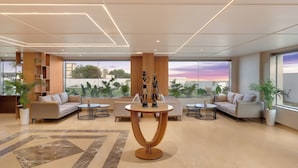 A spacious lobby with a modern design, featuring a central round table, sofas, and potted plants. - Lemon Tree Resort, Somnath (Veraval)