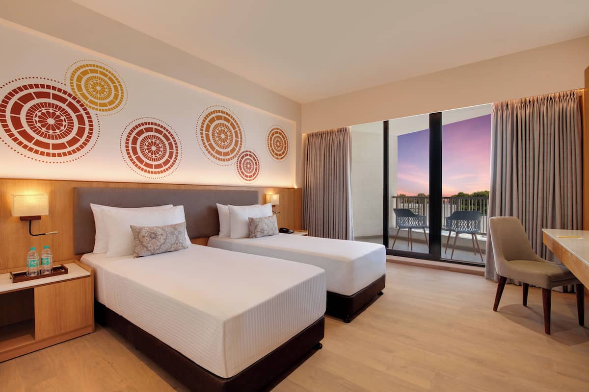 A hotel room with two beds, a desk, and a view of the outdoors.