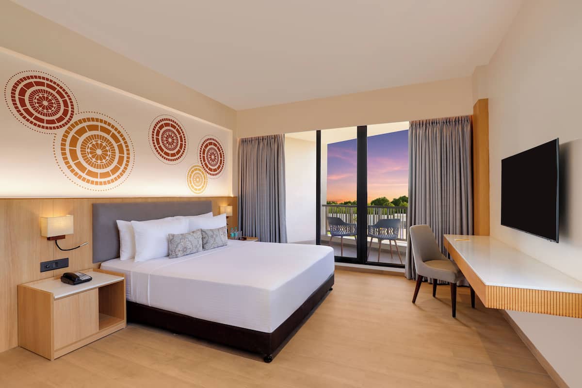 A hotel room with a large bed, a desk, a TV, and a balcony with curtains.