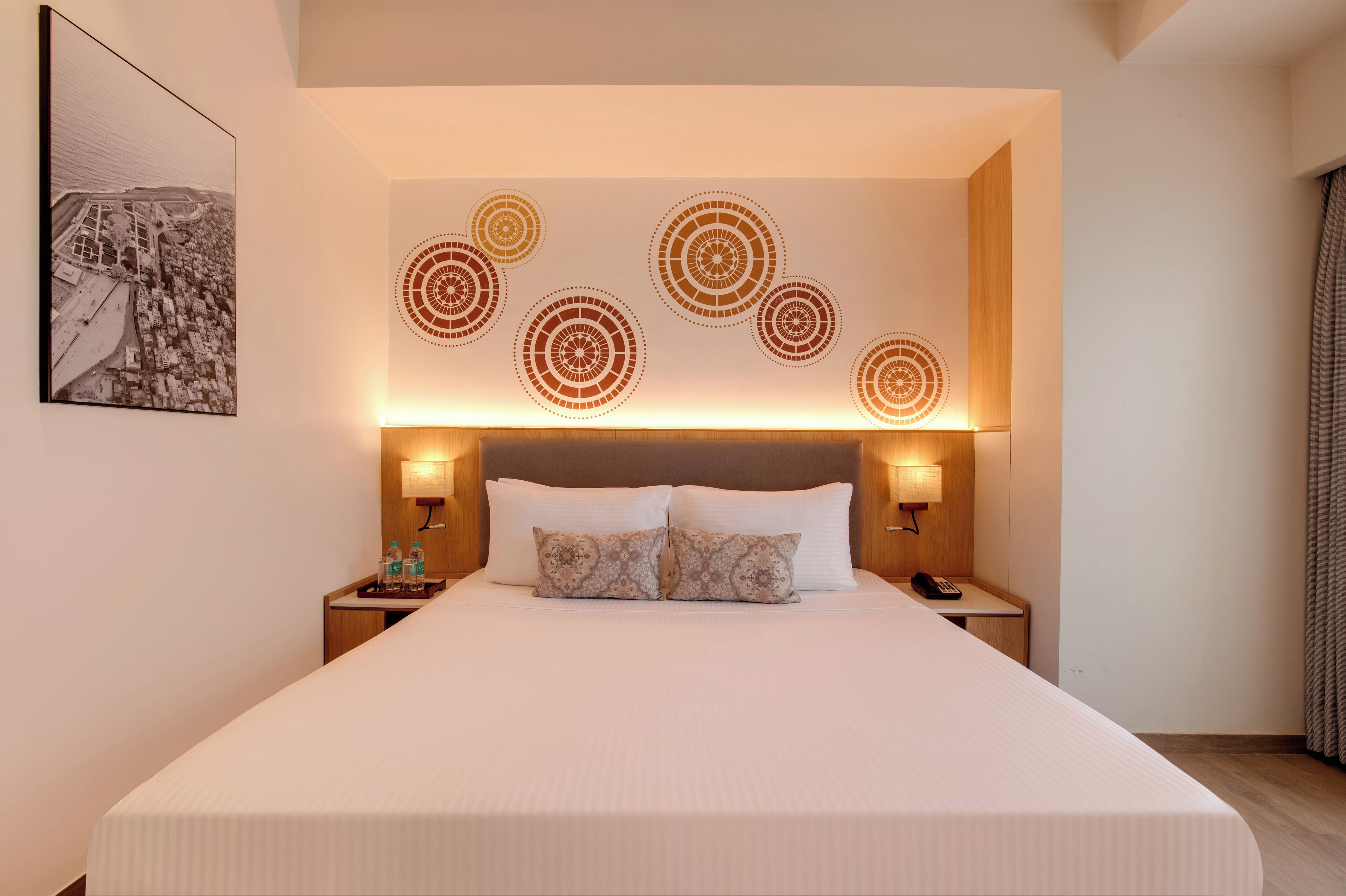 A hotel room with a large bed, two bedside tables, a headboard with circular wall art, and a framed picture on the wall.