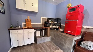 A compact kitchen with white cabinets, a red refrigerator, and a wooden countertop.
