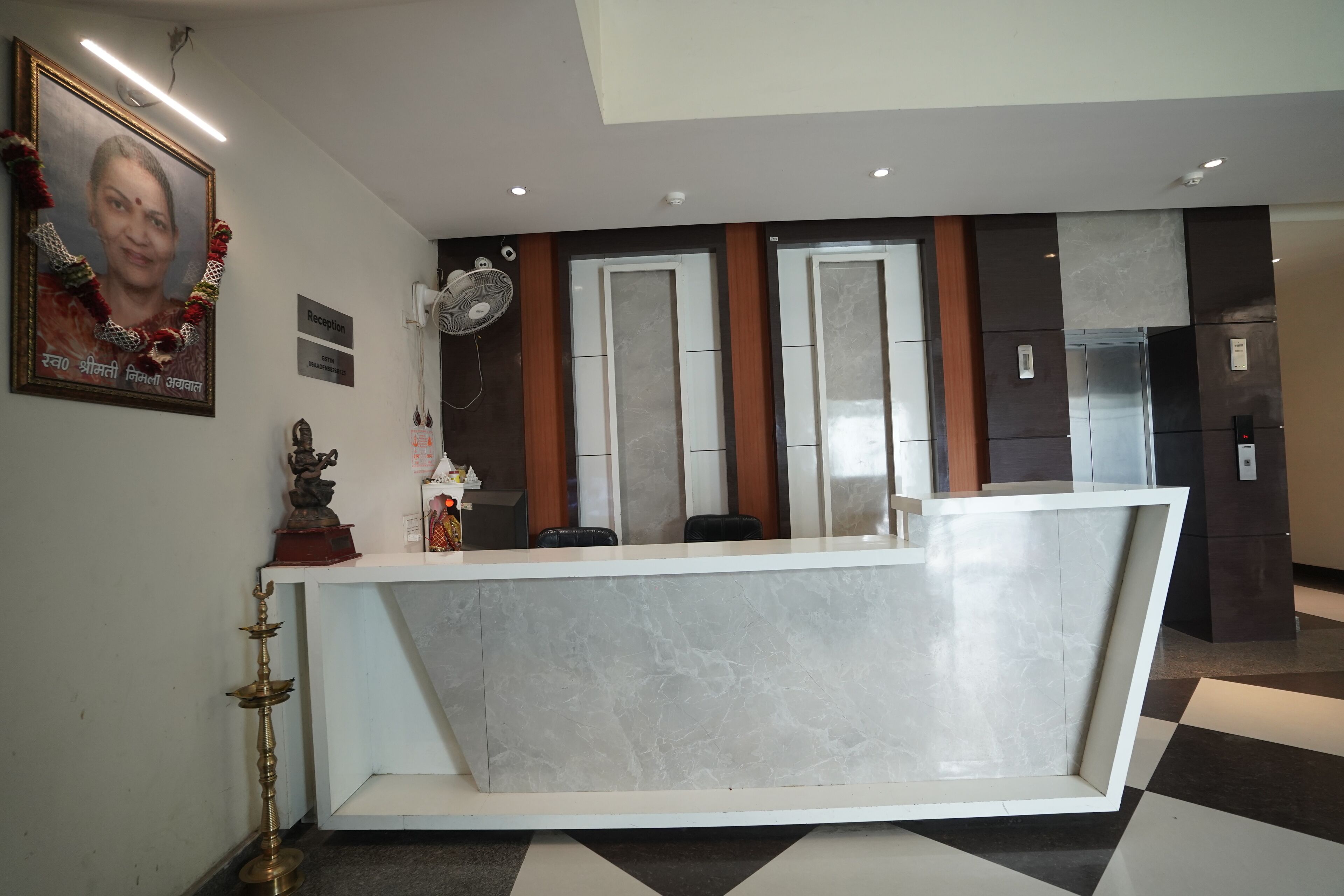 A reception area with a marble counter, a framed portrait, a statue, and a wall-mounted fan.