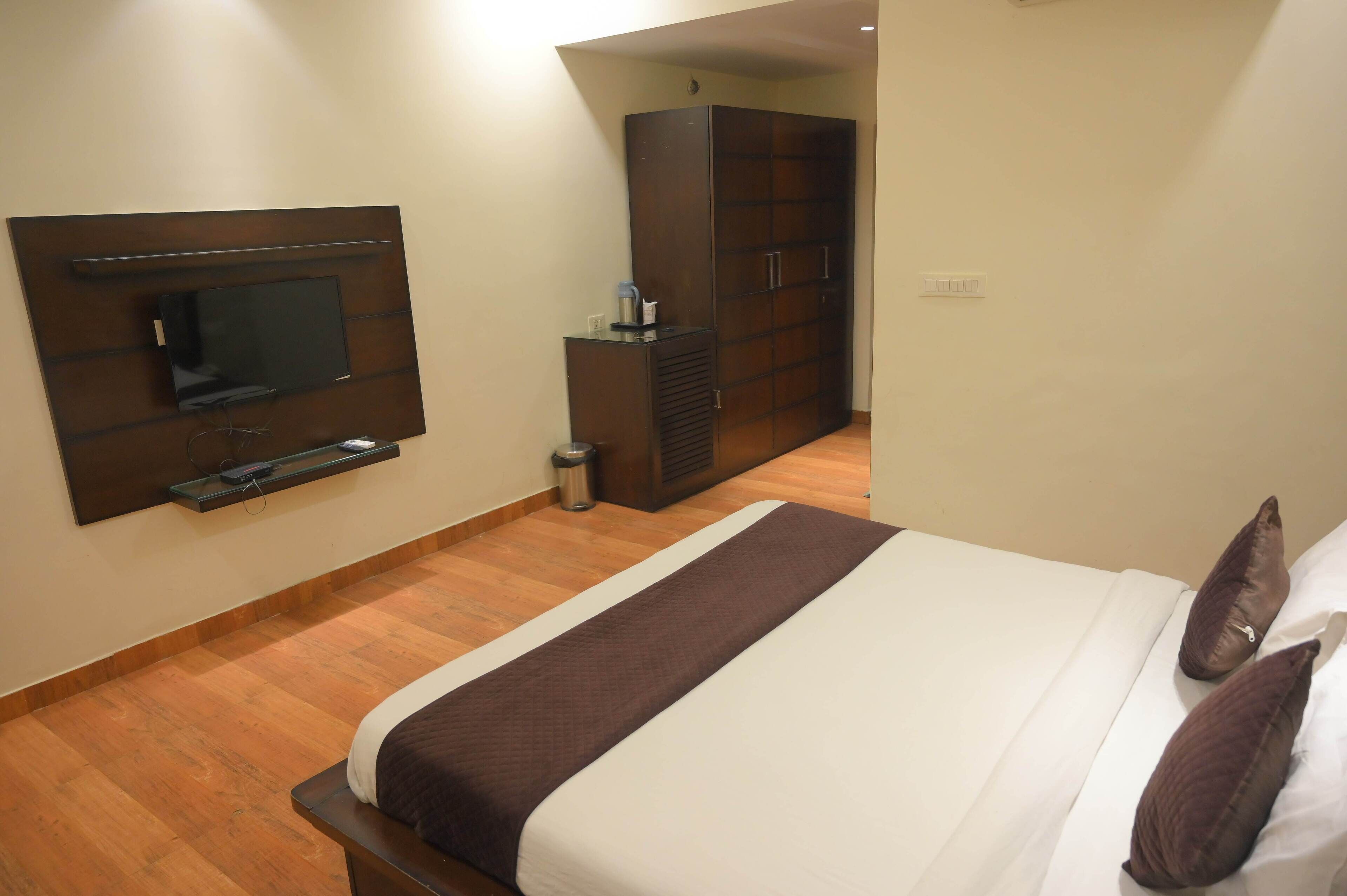 Habitación de hotel con cama, televisor montado en la pared, armario y cubo de basura.