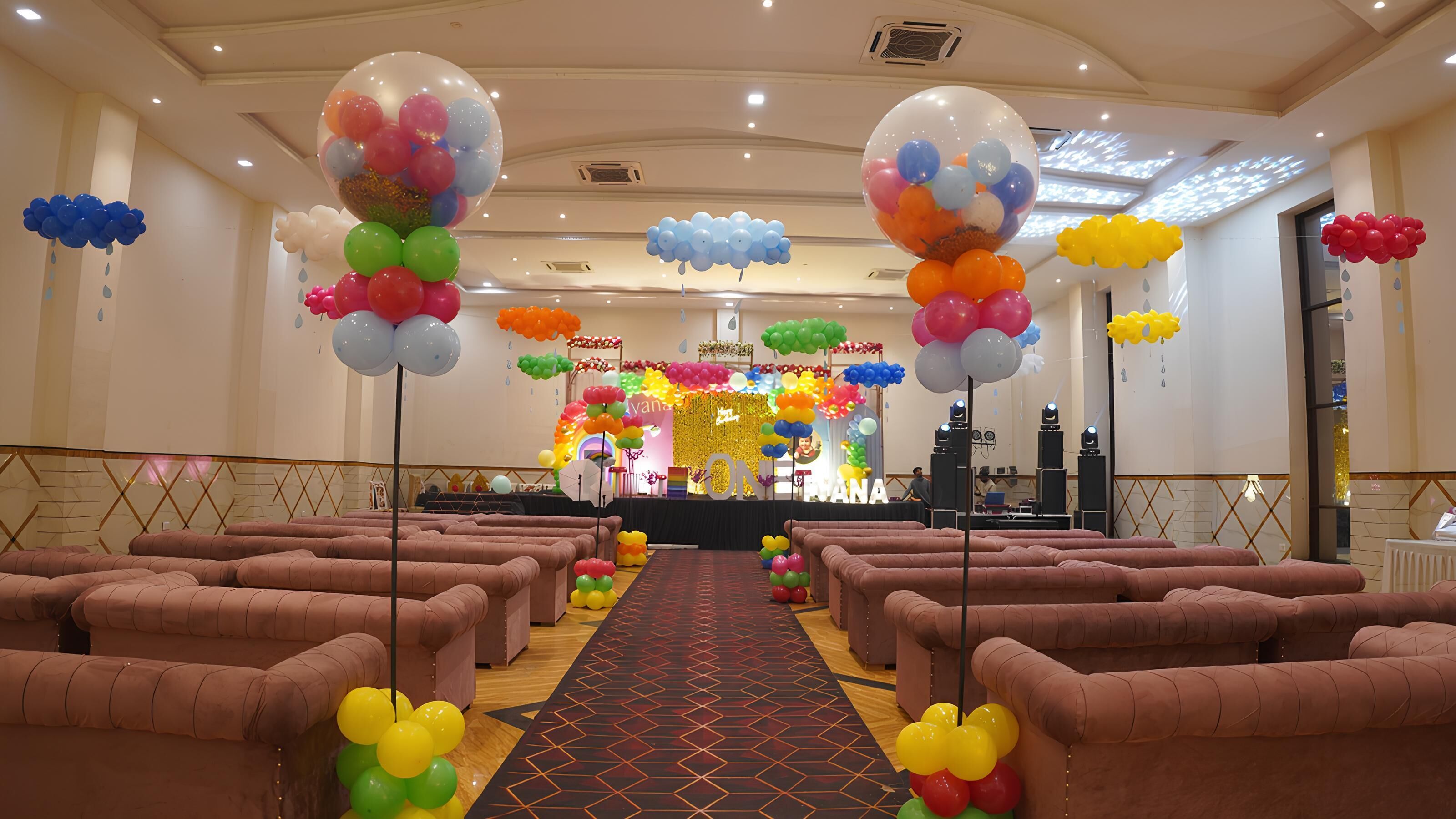 A hotel lobby with a central stage, rows of seating, and colorful balloon decorations.