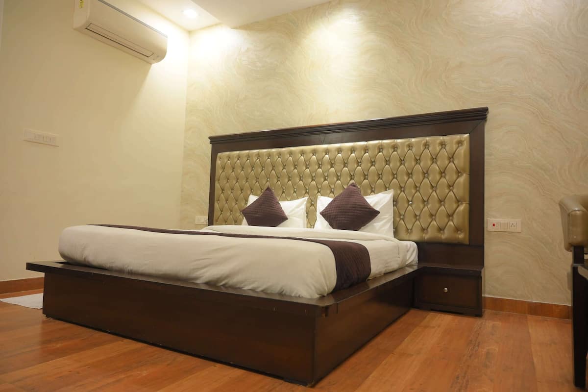 A neatly made bed with a tufted headboard, a bedside table, and a wall-mounted air conditioner.