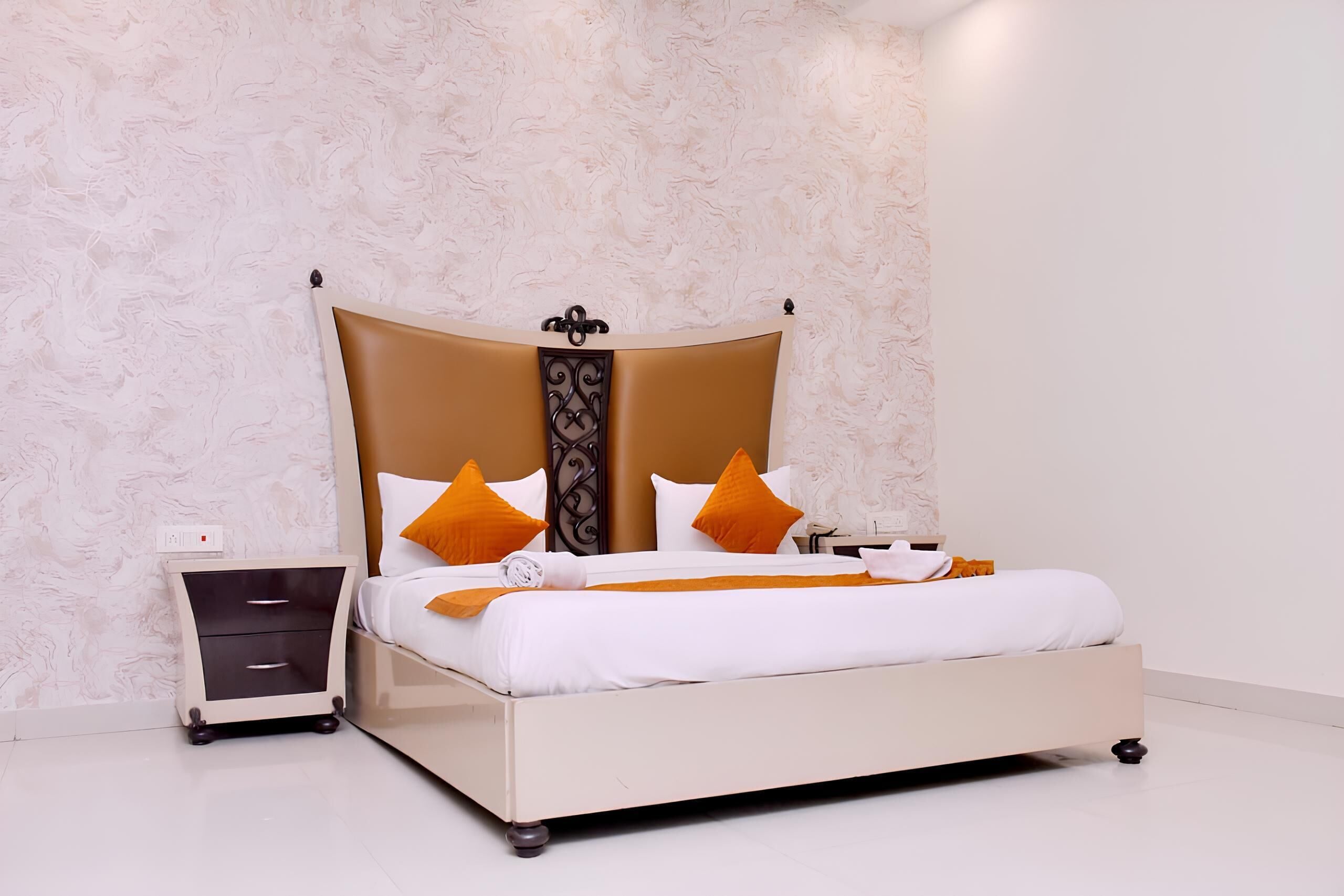 A neatly made bed with a headboard, a bedside table with drawers, and a wall with a textured pattern.