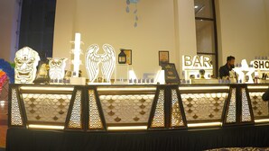 A bar area with a decorative counter, framed artwork, and a bartender. - Nirmal Resort (Bareilly)