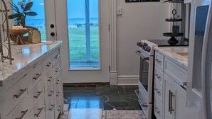 A kitchen with white cabinets, a marble countertop, a stove, and a view of the ocean through a glass door.