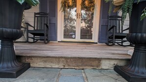A porch with a wooden ceiling, a door with glass panels, and two large planters with greenery.