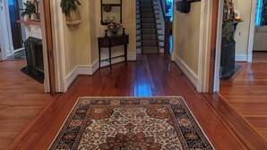 A spacious hallway with a large ornate rug, a chandelier, and a staircase leading to another level.
