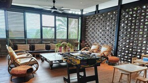 A spacious room with a foosball table, comfortable seating, and large windows. - Talula Hill Farm Resort  (Kluang)
