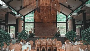 A spacious dining area with wicker chairs and tables, large windows, and hanging wicker light fixtures. - Talula Hill Farm Resort  (Kluang)