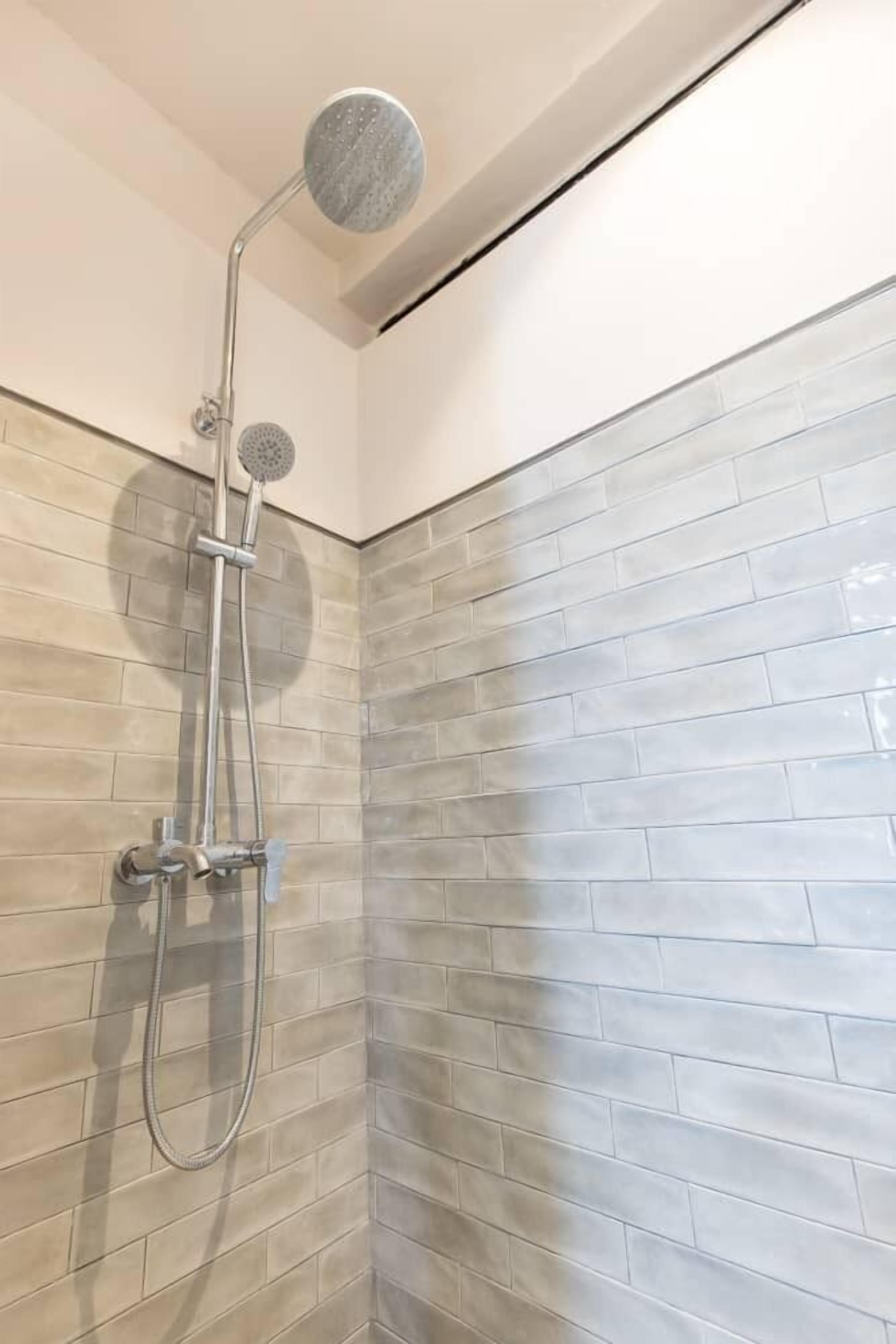 A shower with a handheld showerhead and a wall-mounted faucet.