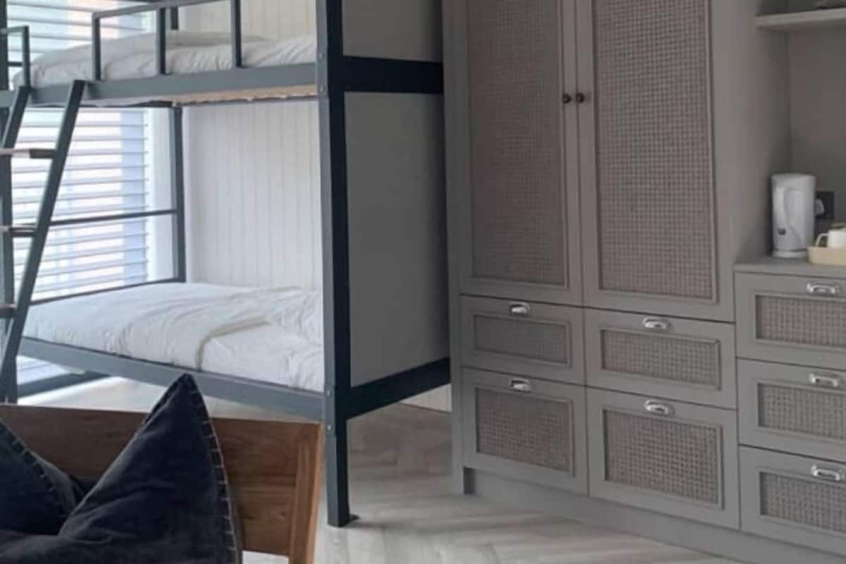 A bunk bed with a ladder, a wardrobe with multiple drawers, and a coffee maker on a shelf.