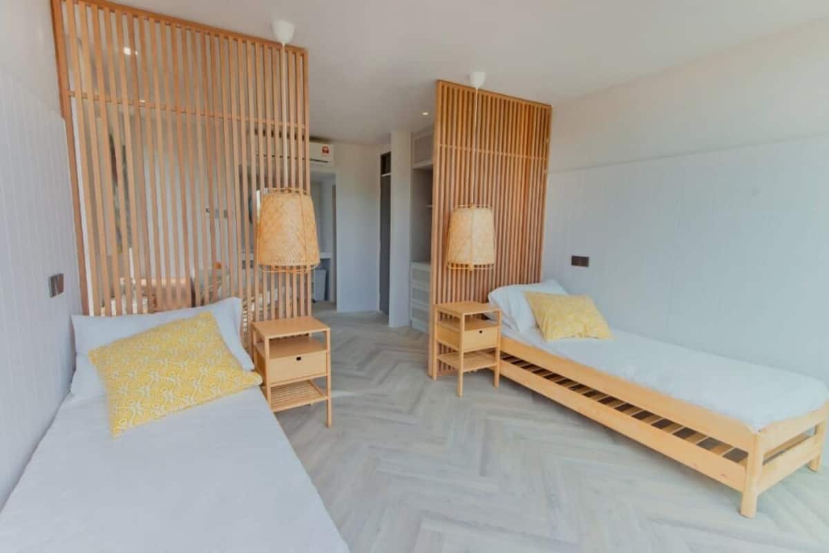 A room with two beds, a wooden floor, and a partition with vertical slats.