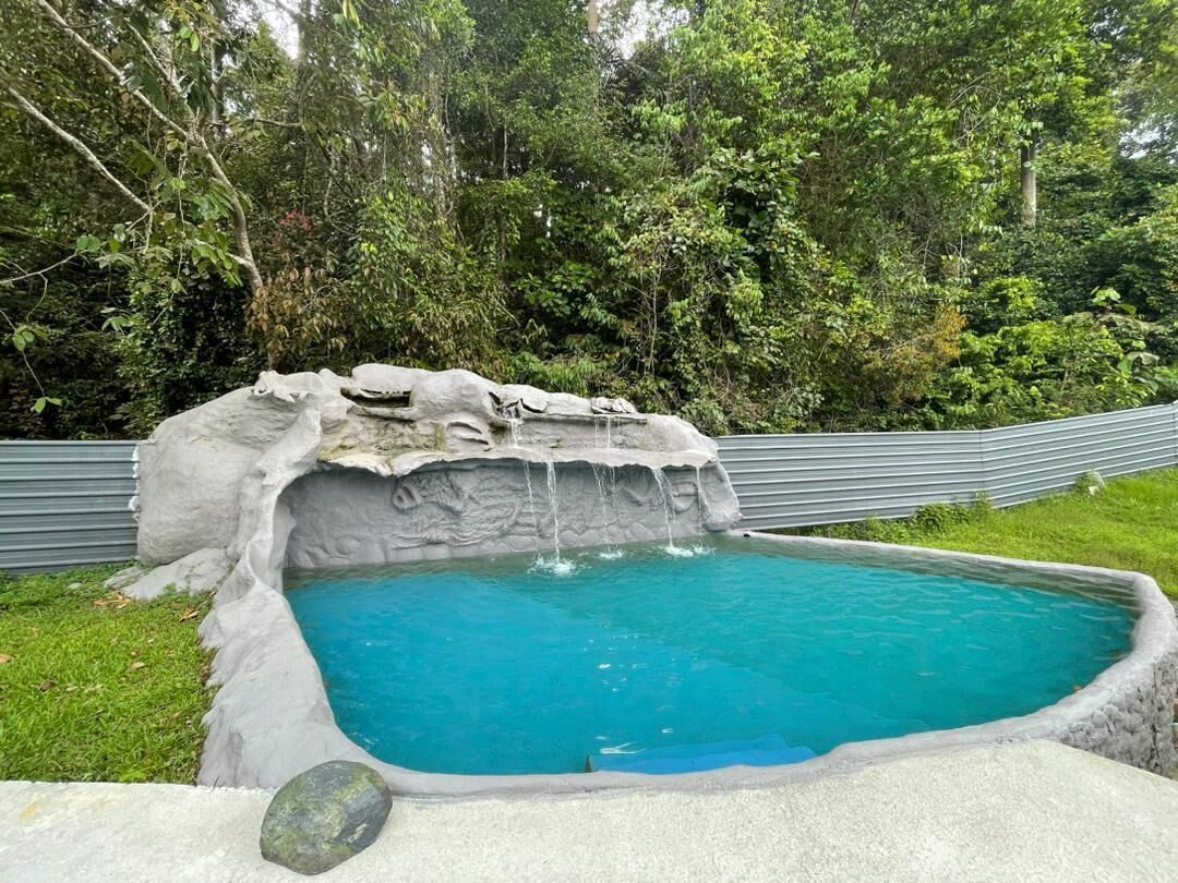 A swimming pool with a waterfall feature surrounded by lush greenery.