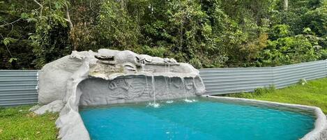 A swimming pool with a waterfall feature surrounded by lush greenery.