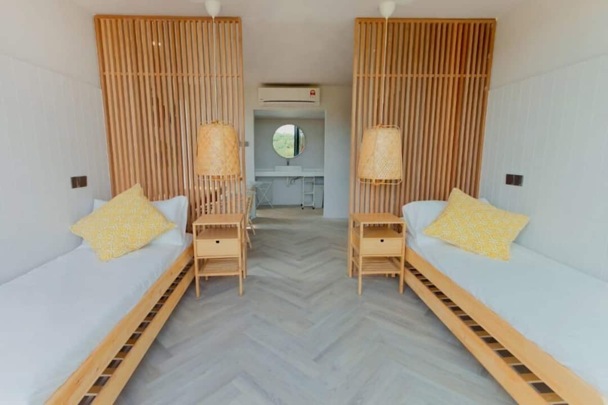 A room with two beds, each with a wooden frame and a yellow pillow. There is a small table between the beds, and a mirror above the table.