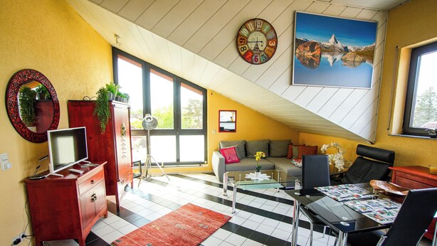 Ein Wohnzimmer mit Schachbrettmuster-Boden, einer Couch, einem Couchtisch, einem Fernseher auf einer Holzkommode und einem großen Fenster.