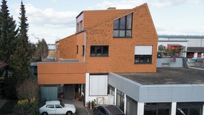 Ein modernes Gebäude mit geneigtem Dach, einer Garage und einem Parkplatz mit zwei Autos.