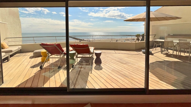 Un balcó amb vista a la platja, gandules i una taula amb cadires.