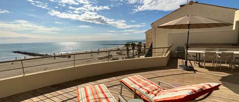 Un balcón con sillones de descanso y una mesa, con vistas a una playa y al mar.